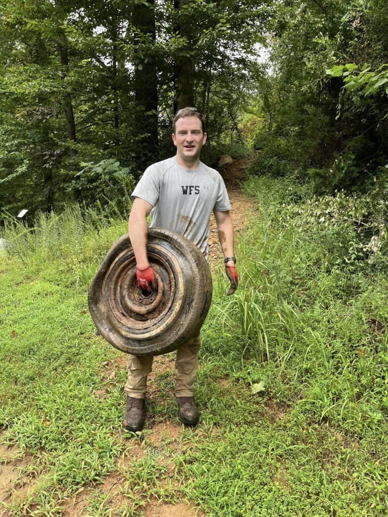 A man holds an old wheel while cleaning up the forest.